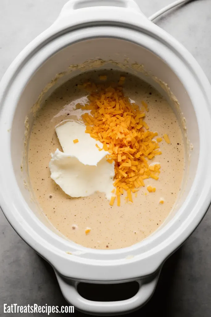 Cream cheese and shredded cheddar melting in creamy potato soup inside crock pot