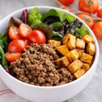 Whole 30 ground beef and potato taco bowl with fresh vegetables on white marble background