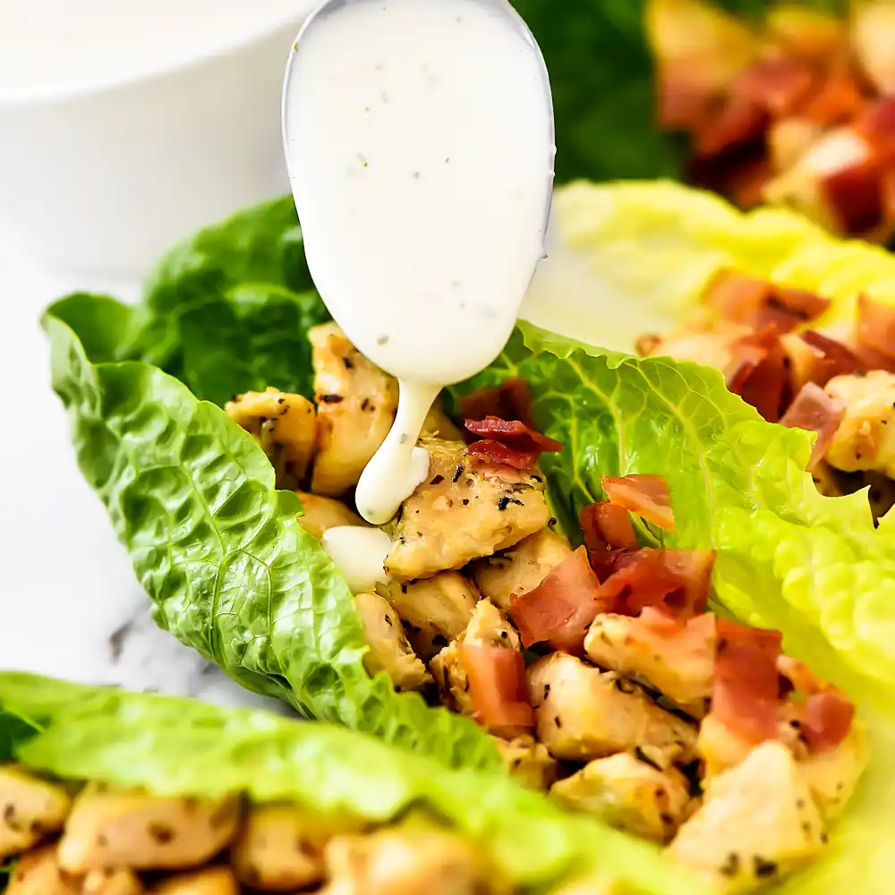 Chicken bacon ranch lettuce wraps ingredients including shredded chicken, crispy bacon, ranch dressing, cheese and romaine lettuce on white marble background