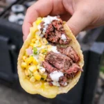 Grilled Steak Elote Tacos served on white marble background with cotija cheese and lime wedges
