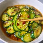 Serving Asian cucumber salad in white bowl with sesame seeds and chili oil