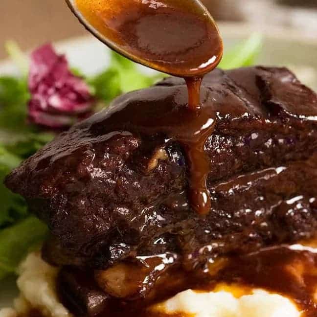 Raw beef short ribs with carrots, garlic, herbs, and wine on marble surface