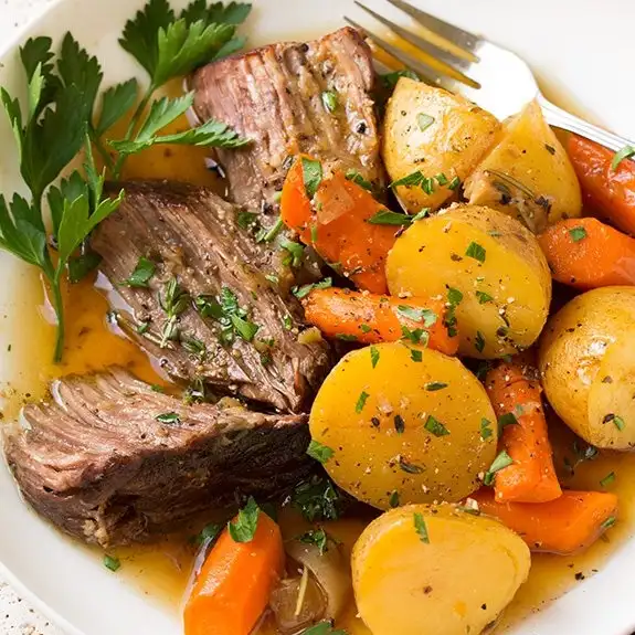 chuck roast and potatoes cooking inside crock pot slow cooker