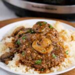 Serving crockpot beef patties and mushrooms with gravy on white plate