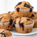 Serving high protein blueberry muffins on white plate with fresh blueberries