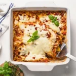 A bubbling hot dish of high protein ratatouille lasagna with golden melted cheese on a wooden dining table.