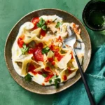 Family style platter of mushroom manti with garlic yogurt and tomato sauce on a white marble background.