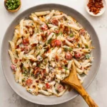 A wide ceramic bowl filled with traditional creamy million dollar pasta salad on a bright white marble background.